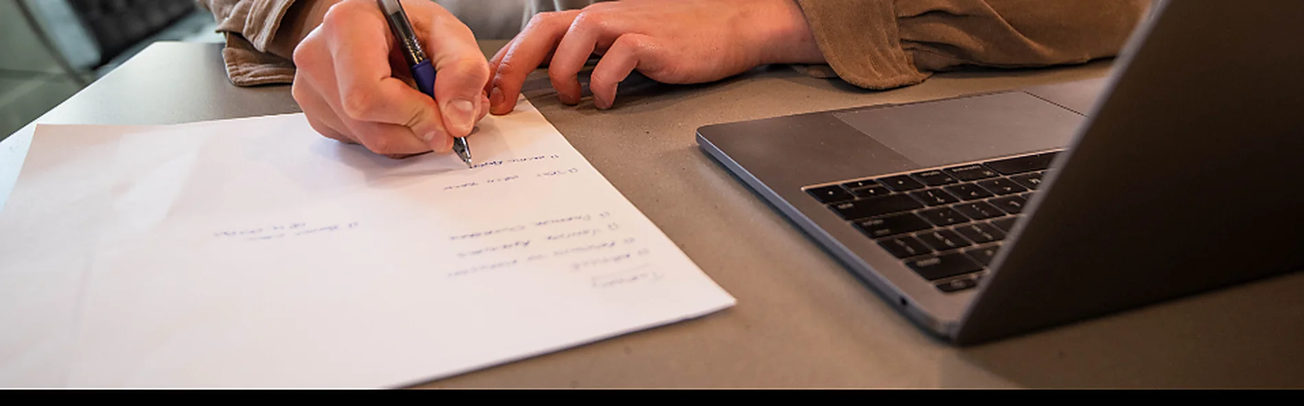 A student writing notes beside a laptop